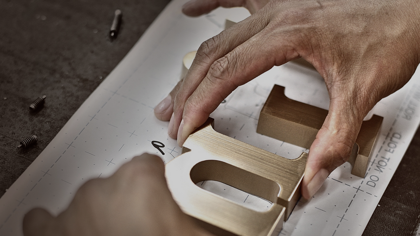 Closeup of hands placing a cast metal letter on a drill pattern.