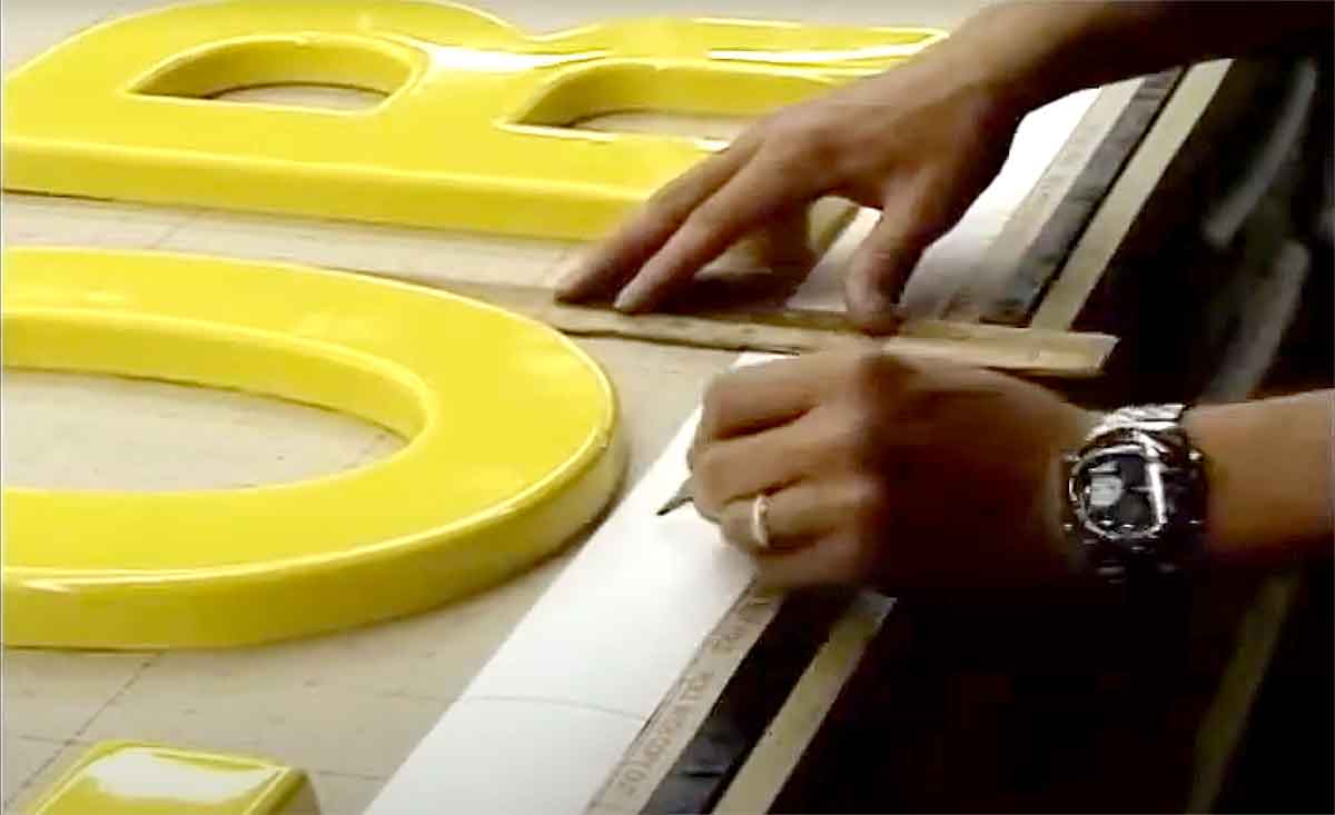 A worker creating a spacing guide to assist with the installation of sign letters.