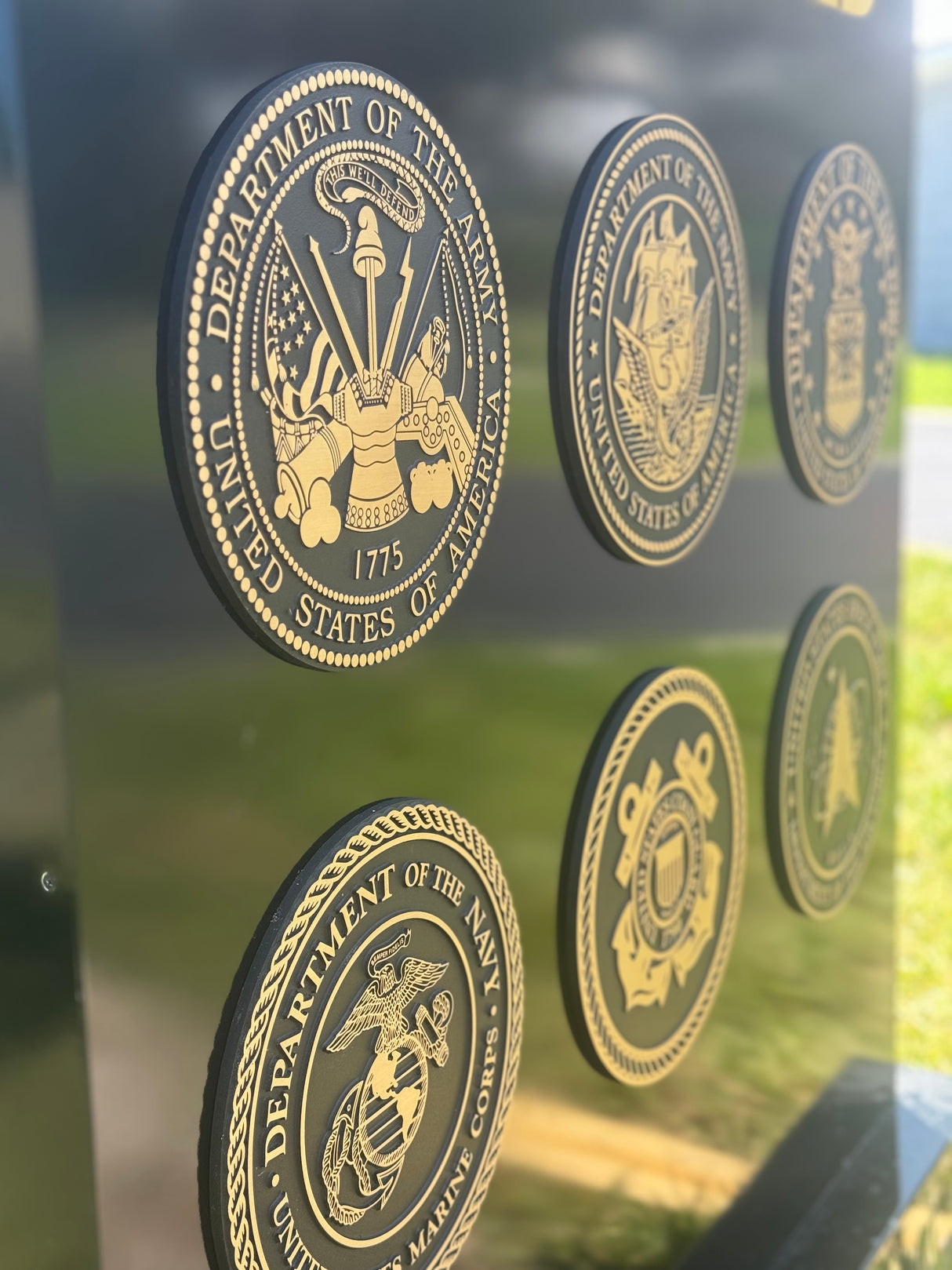 Multiple solid bronze military seals on a reflective surface with a blurred outdoor background.