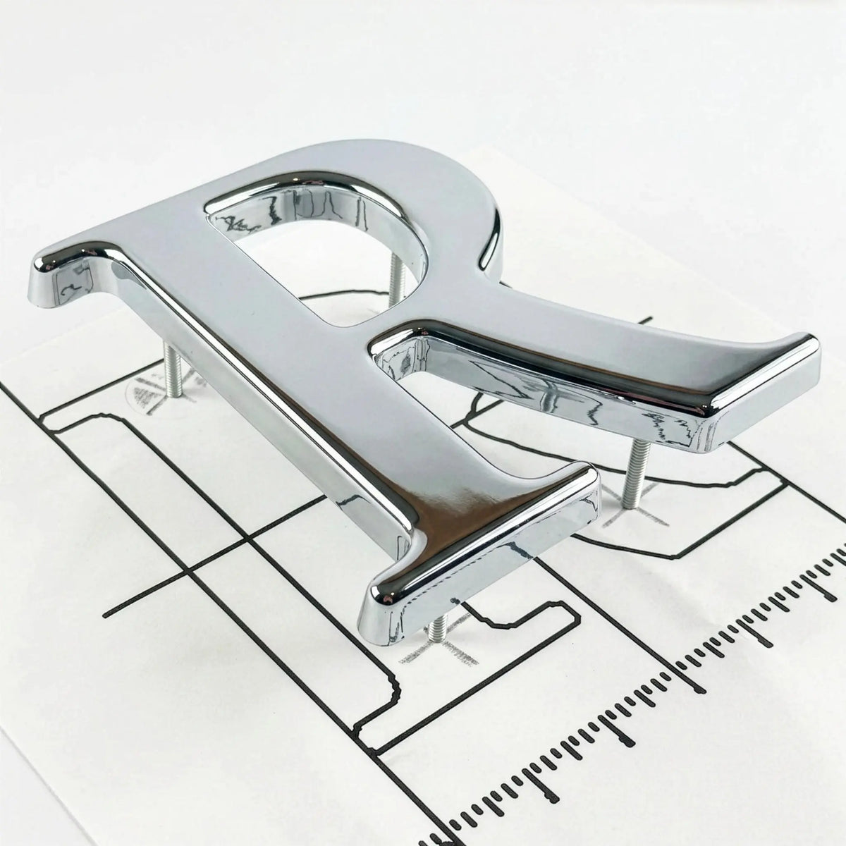 A polished chrome letter 'R' on an installation template with mounting studs.