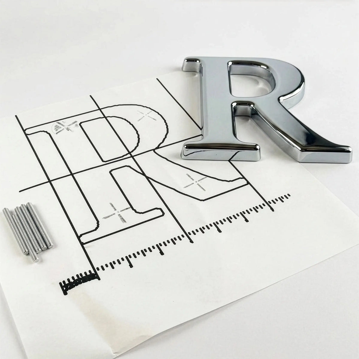 A polished chrome letter 'R' on an installation template with mounting studs.