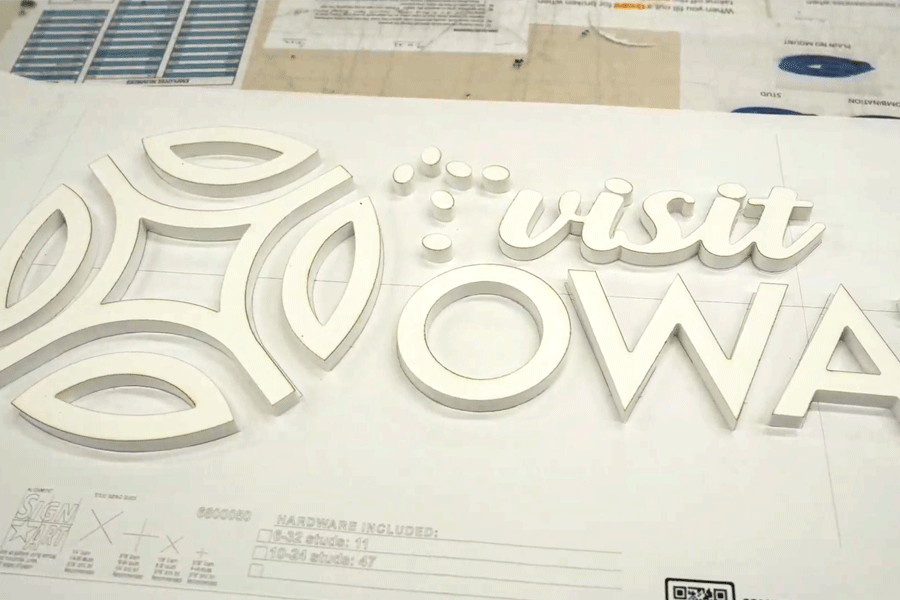 Flat cut acrylic sign letters arranged on a drill pattern mounting guide.