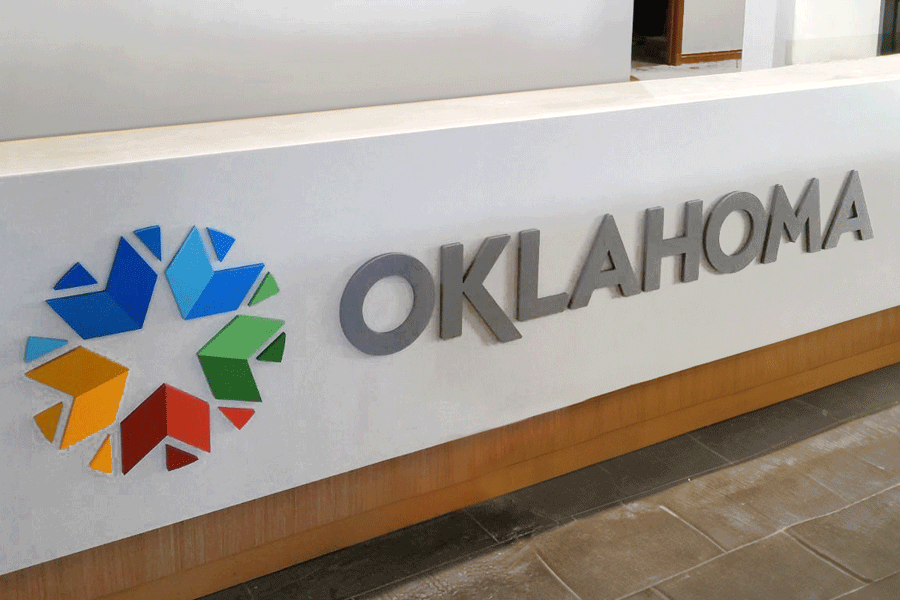 A reception desk sign for the state of Oklahoma with a multi-colored acrylic logo and silver painted acrylic sign letters.