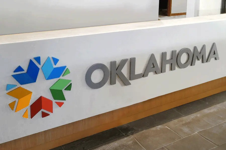 A reception desk sign for the state of Oklahoma with a multi-colored acrylic logo and silver painted acrylic sign letters.