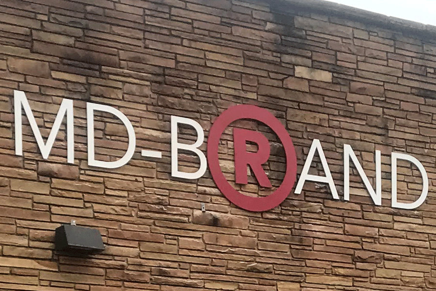 An exterior wall sign for MD Brand with white and red acrylic sign letters.