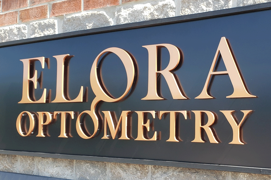 An exterior wall sign for Elora Optometry with bronze painted acrylic letters on a black background.