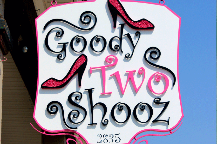 A hanging store sign for Goody Two Shooz with pink and black acrylic sign letters and a pair of fancy pink high-heeled shoes