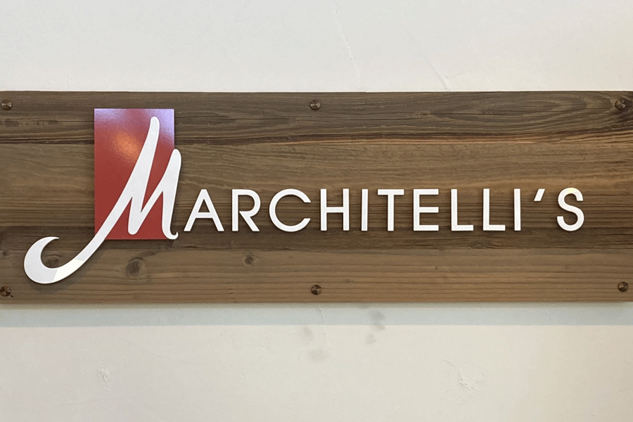 A lobby sign with white flat cut acrylic sign letters and a logo with the letter M inside a red square.