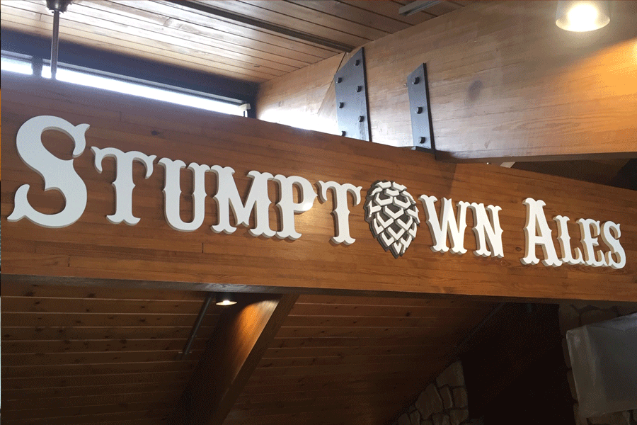 Custom flat cut acrylic building sign with white sign letters and a pine cone shape in place of a letter O.