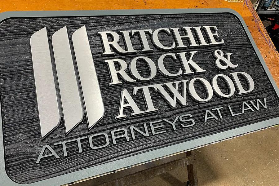 Law office sign with brushed aluminum sign letters on a black plaque.