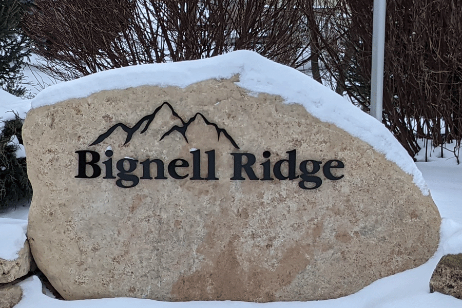 An exterior monument sign on a boulder made of black anodized aluminum sign letters and shapes.