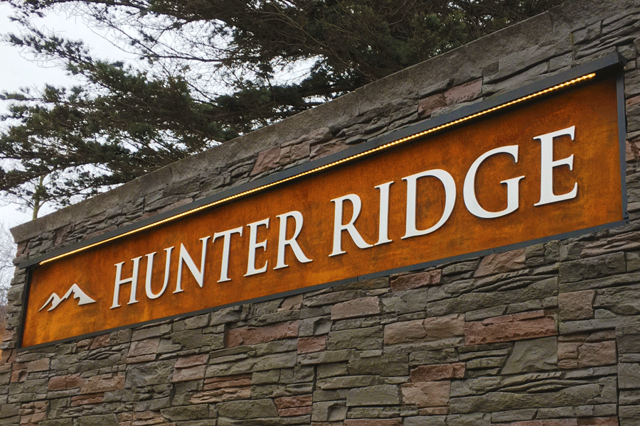 An exterior monument sign with brushed aluminum sign letters on a weathered steel background.