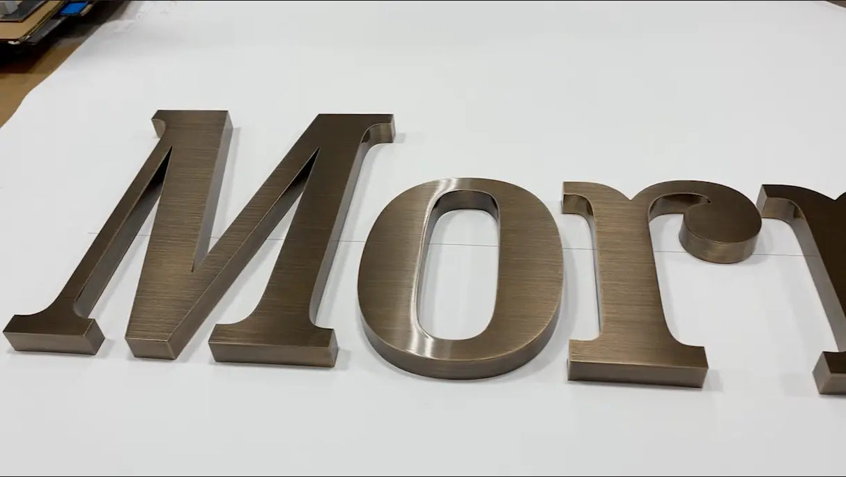 Aged bronze sign letters spelling 'Mory' on a white background
