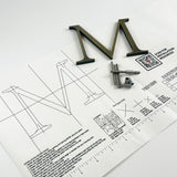 Lightly aged solid brass division 10 architectural sign letter on mounting template with hardware