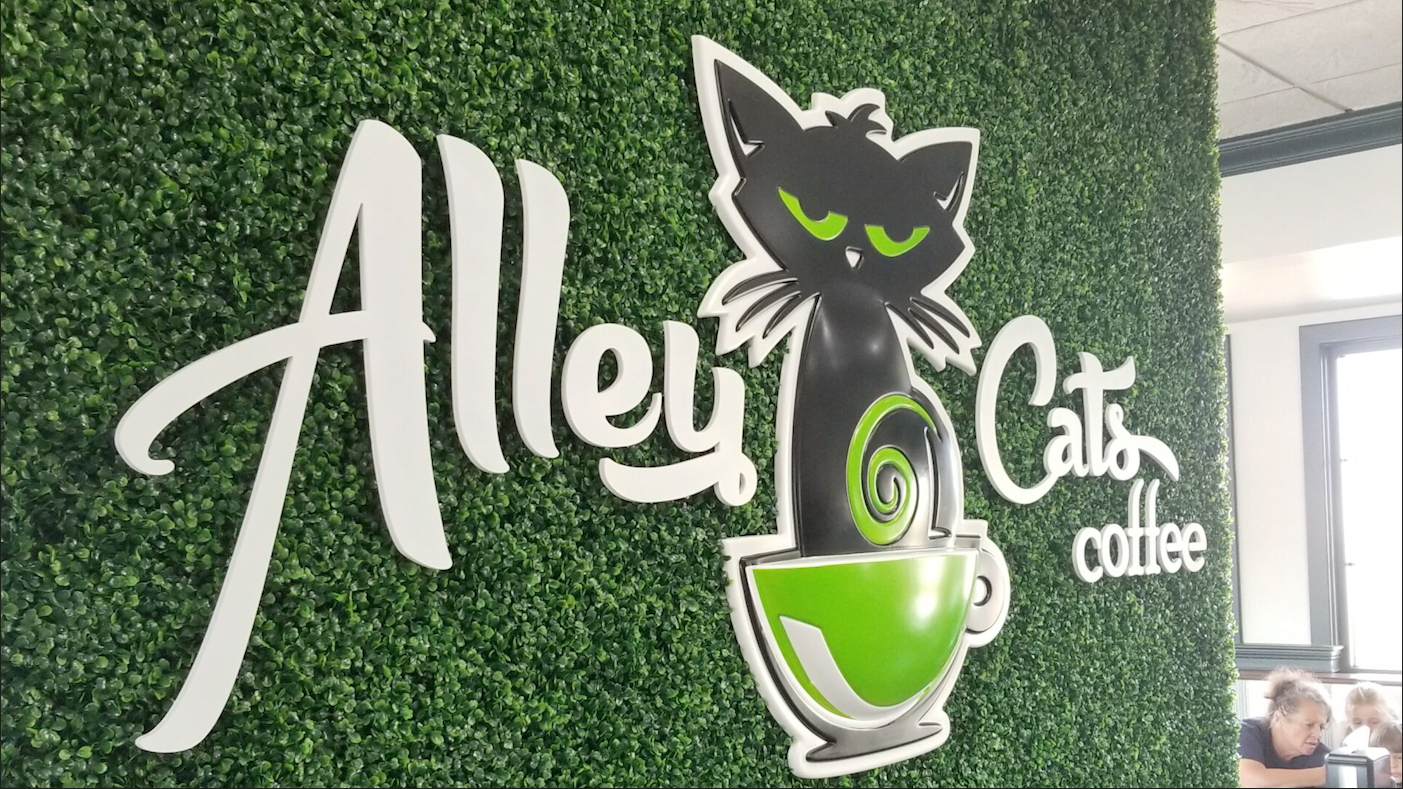 Formed plastic sign of Alley Cats Coffee on a green textured wall with white formed plastic letters and a custom formed logo of a cat in a coffee cup