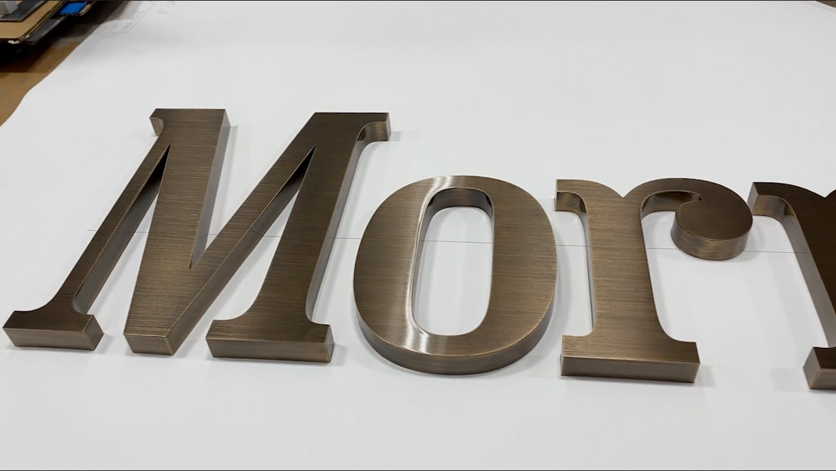 Aged bronze sign letters spelling 'Mory' on a white background