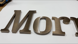 Aged bronze sign letters spelling 'Mory' on a white background